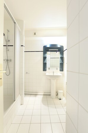 Een badkamer met een douche met glazen wand, een wit wastafelmeubel en een spiegel met zwarte lijst.