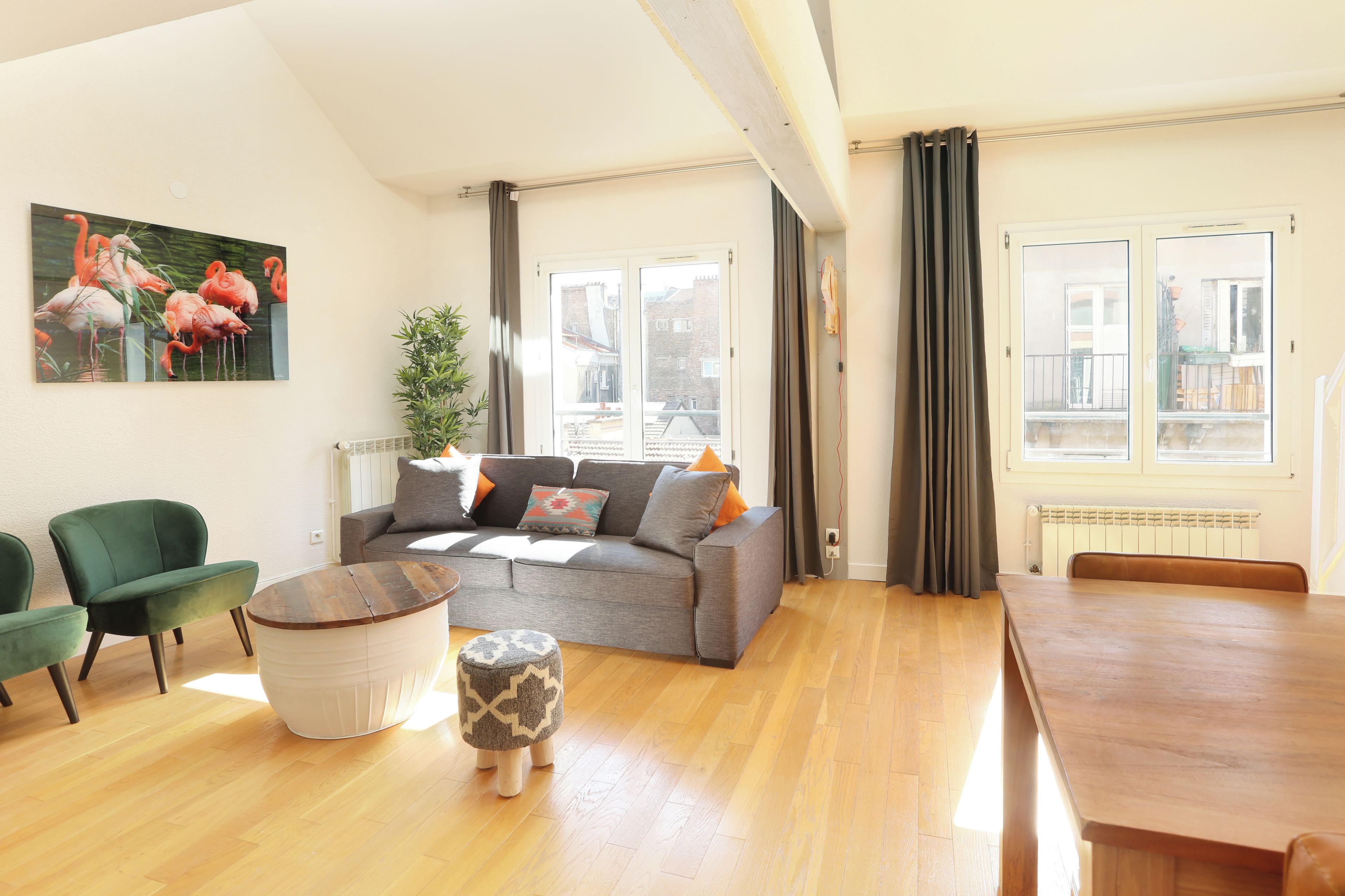 A living room with a grey sofa, green armchairs, a wooden coffee table, and a dining table.