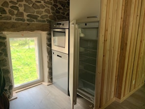 A compact kitchen with a stone wall, a built-in oven, and a refrigerator. - La Grange de la Gratade: a vacation rental where you can reconnect, recharge, and explore (Rochefort-Montagne)