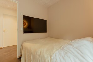 A bedroom with a large bed, a flat-screen TV mounted on the wall, and a door leading to another room.