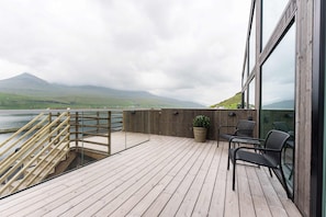 A wooden deck with a view of a lake and mountains, a staircase, and outdoor seating.