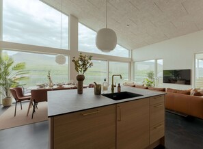 Eine moderne Küche mit einer großen Kochinsel, einem Essbereich mit Aussicht und einem Wohnbereich mit Sofa und Fernseher.