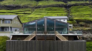 Een modern gebouw met grote glasramen, een houten terras en een trap naar een balkon.