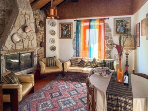 Un saló acollidor amb una llar de pedra, un conjunt de sofàs, una catifa amb dibuixos i una taula amb una ampolla.