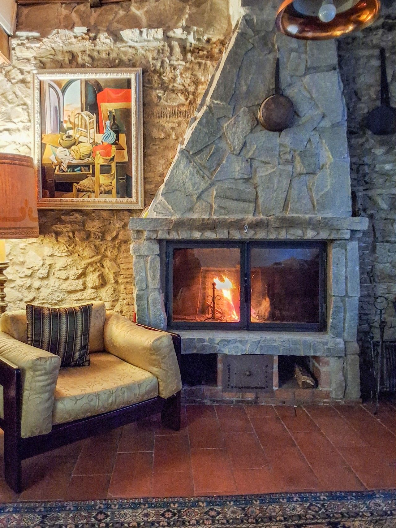 A stone fireplace with a fire, a cushioned armchair, and a framed picture on the wall.