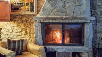 A stone fireplace with a fire, a cushioned armchair, and a framed picture on the wall.