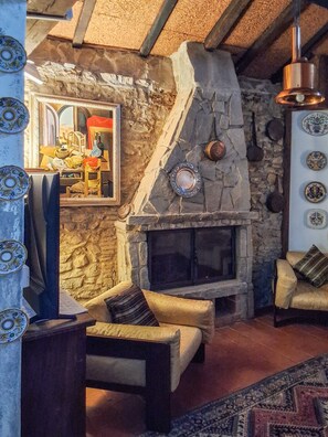Un saló d'estar acollidor amb una llar de pedra, seients confortables i plats decoratius a la paret.