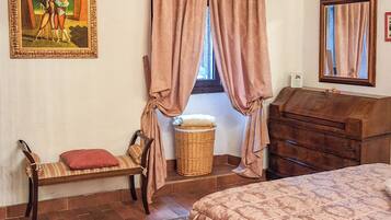 A bedroom with a bed, a wooden dresser, a chair, a wicker basket, and a painting on the wall.