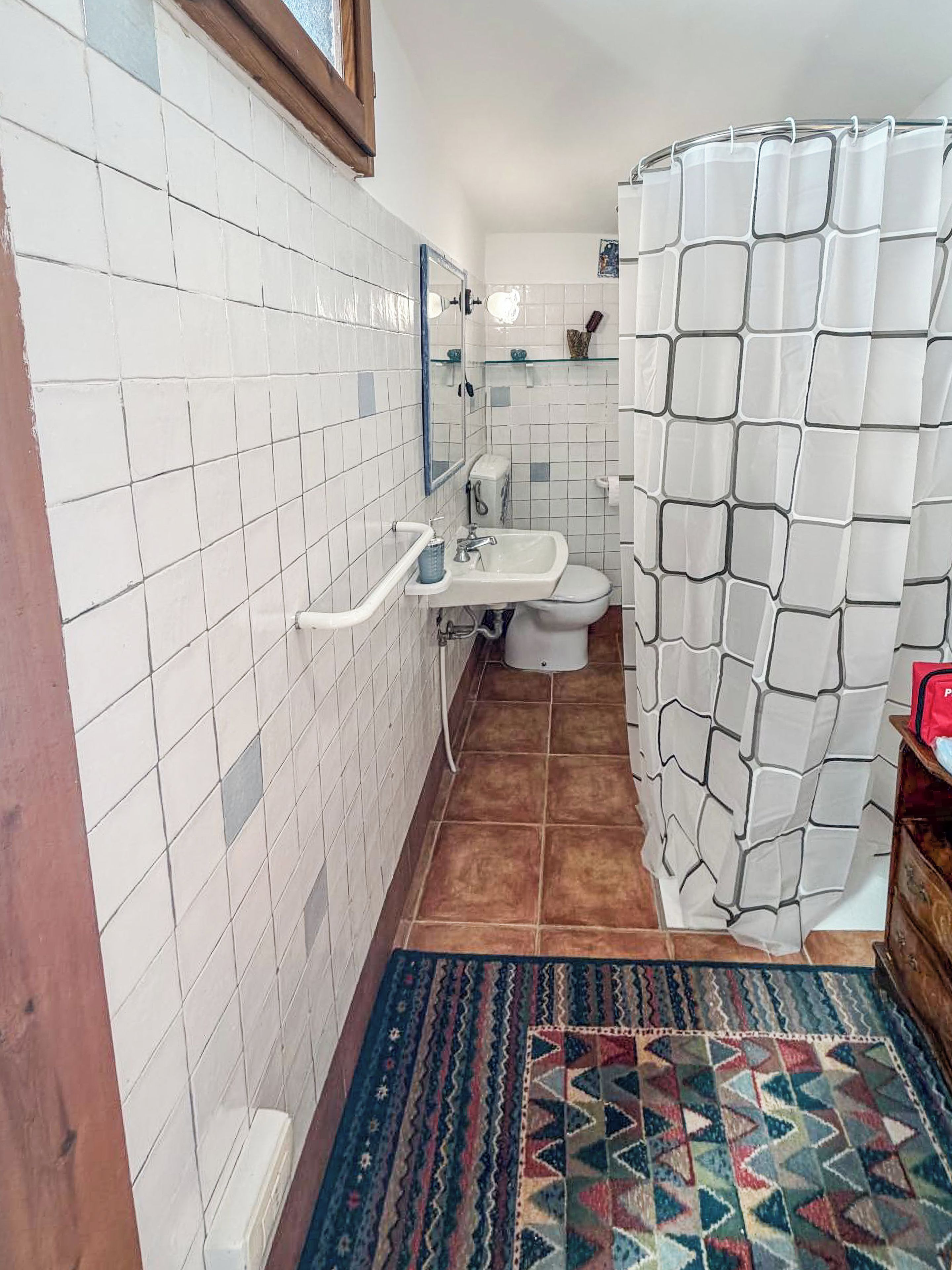 Une salle de bain avec des murs recouverts de carreaux blancs, un lavabo, des toilettes et un rideau de douche.
