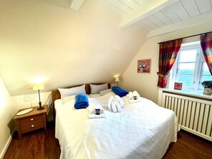 A hotel room with a bed, bedside tables, a lamp, a window with curtains, and a radiator. - Deichhof Apt. 22 (Dunsum)
