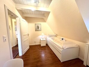 Una habitación pequeña y luminosa con una cama individual, una mesita de noche y un ventilador de techo.