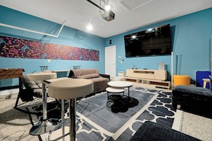A modern living room with a blue wall, a large flat-screen TV, a ceiling fan, and a patterned rug. - Magical Moments at Reunion Village Retreat (Kissimmee)