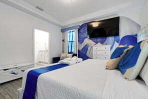 A hotel room with a large bed, a flat-screen TV mounted on the wall, a white dresser, and a window with blue curtains. - Magical Moments at Reunion Village Retreat (Kissimmee)