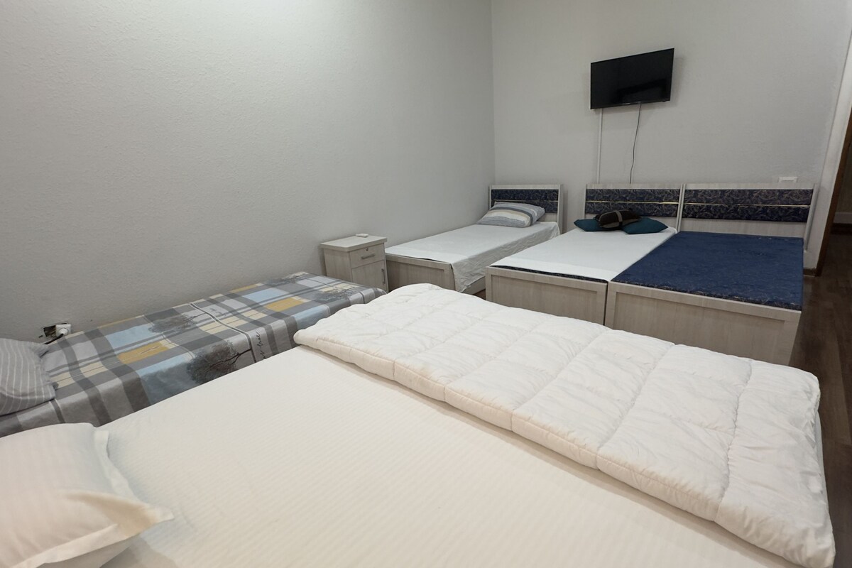 A hotel room with a large bed, a smaller bed, a TV mounted on the wall, and a wooden floor.