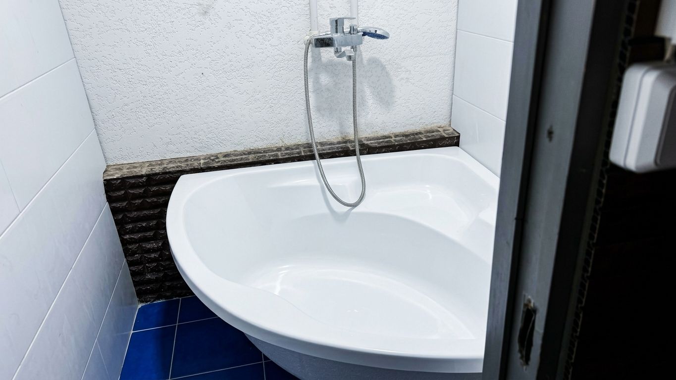 A white pedestal sink with a handheld showerhead in a bathroom with white walls and blue tiles.