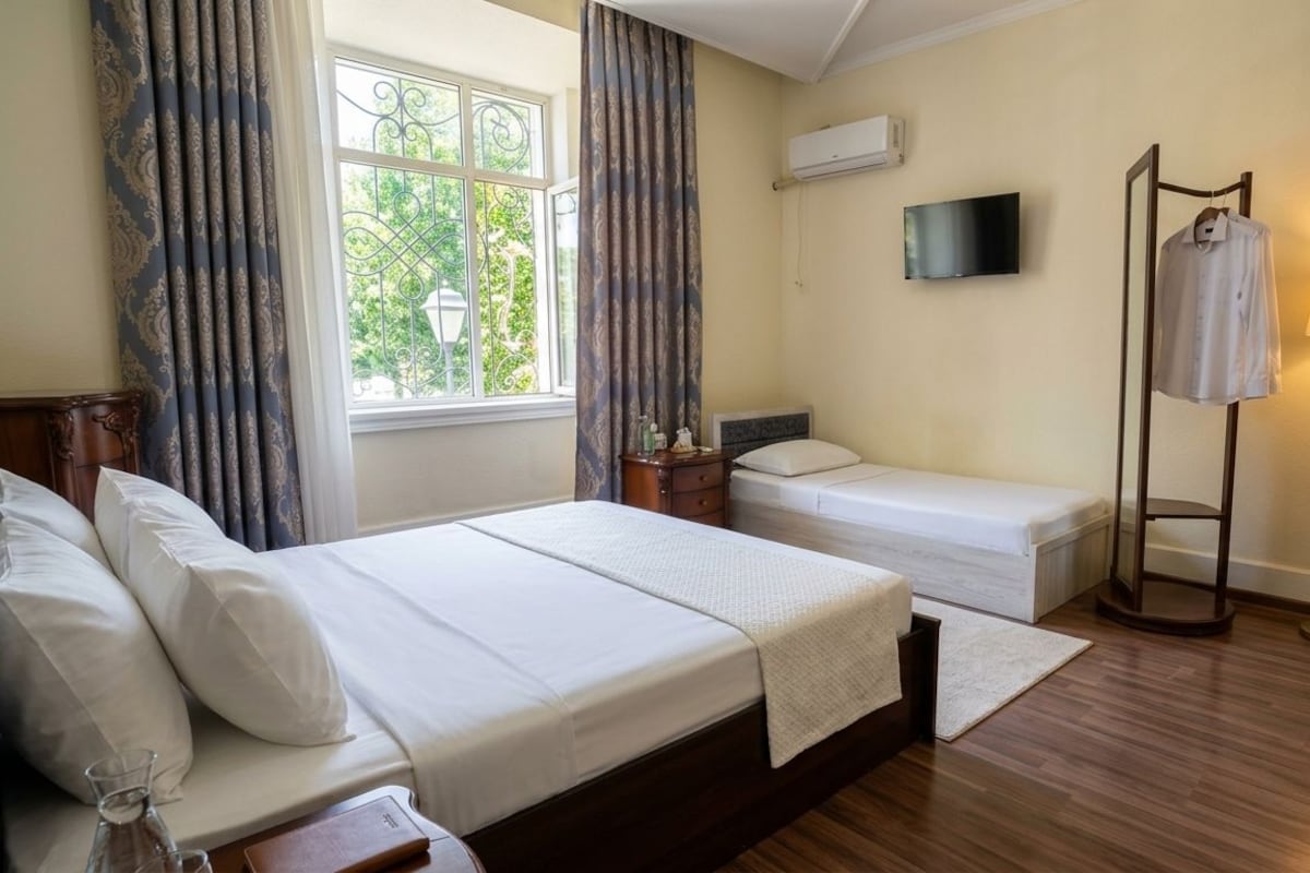 A hotel room with a bed, bedside table, lamp, and a TV on the wall.