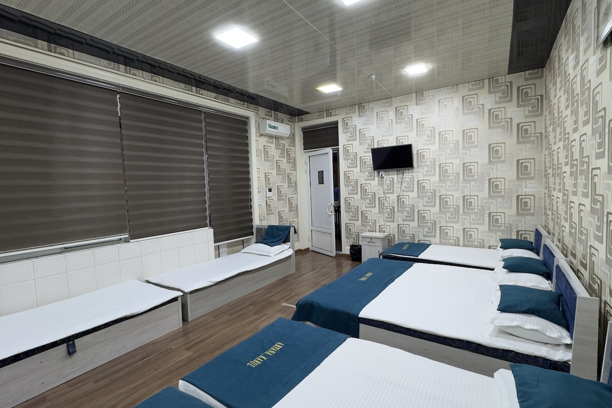 A hotel room with two beds, a television, and a window with blinds.