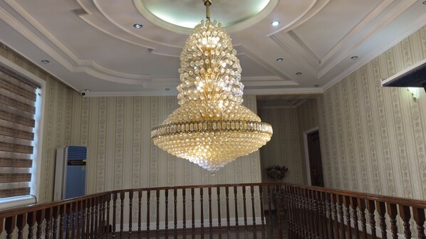 Un gran candelabro con varios niveles de luces, una escalera de madera con balaustres y un interior con papel tapiz estampado.