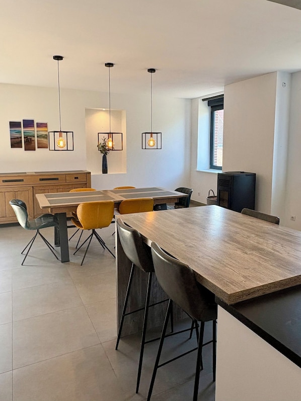 A modern kitchen with a wooden dining table, bar stools, pendant lights, and a built-in stove.