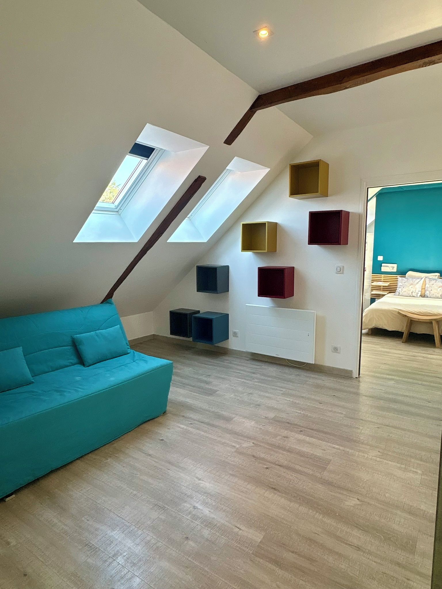 Une chambre à coucher de style loft avec un plafond en pente, des fenêtres de toit, un canapé de couleur turquoise et des rangements intégrés.