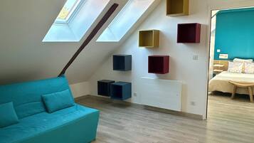Une chambre à coucher de style loft avec un plafond en pente, des fenêtres de toit, un canapé de couleur turquoise et des rangements intégrés.