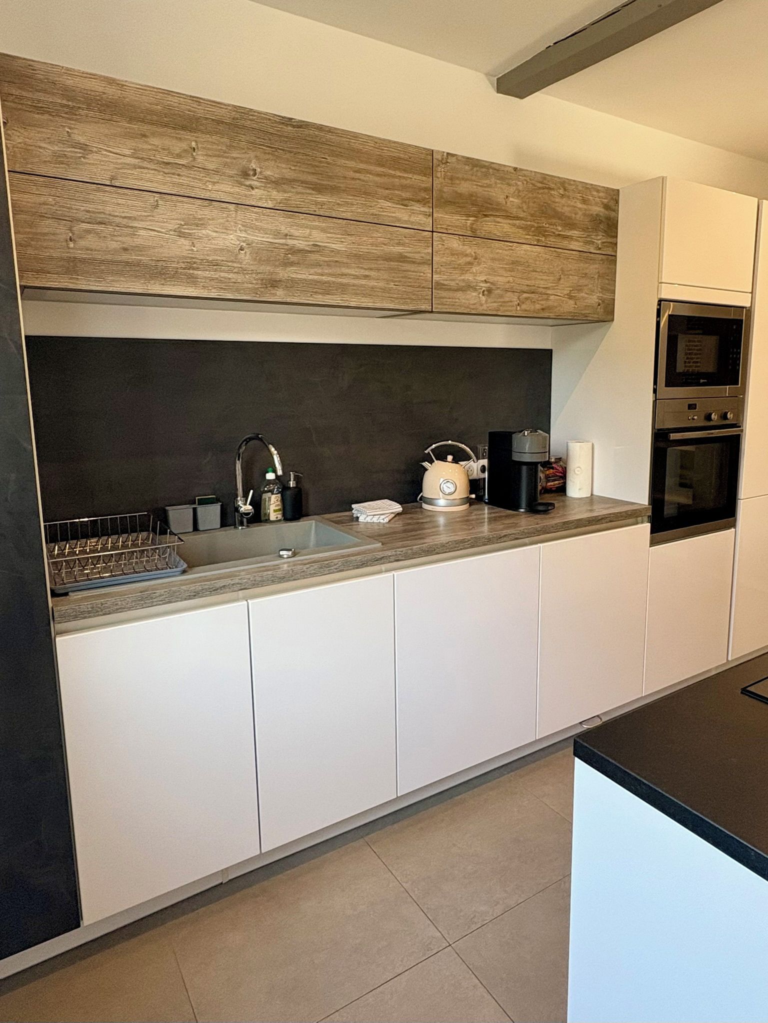 Une cuisine moderne avec des meubles blancs, un plan de travail en bois, une bouilloire, une machine à café et un four.