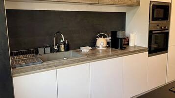 Une cuisine moderne avec des meubles blancs, un plan de travail en bois, une bouilloire, une machine à café et un four.
