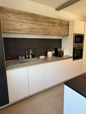 A modern kitchen with white cabinets, a wooden countertop, a kettle, a coffee maker, and an oven.