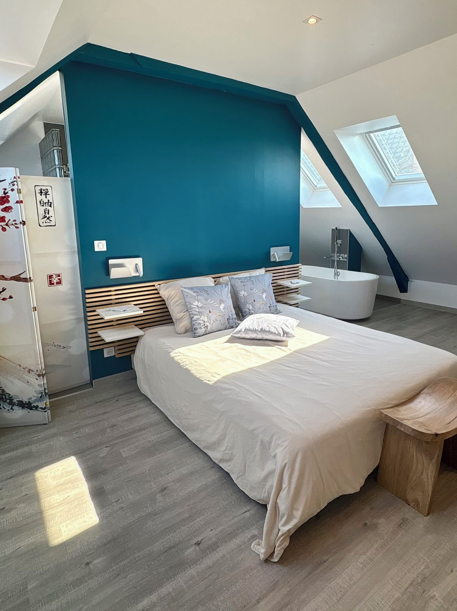 Ein modernes Schlafzimmer mit schrägverdeckter Decke, einem großen Bett, einer integrierten Badewanne und Dachfenstern.