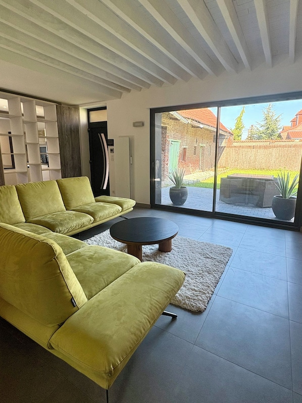 A modern living room with a sectional sofa, a round coffee table, and a large sliding glass door leading to an outdoor patio.