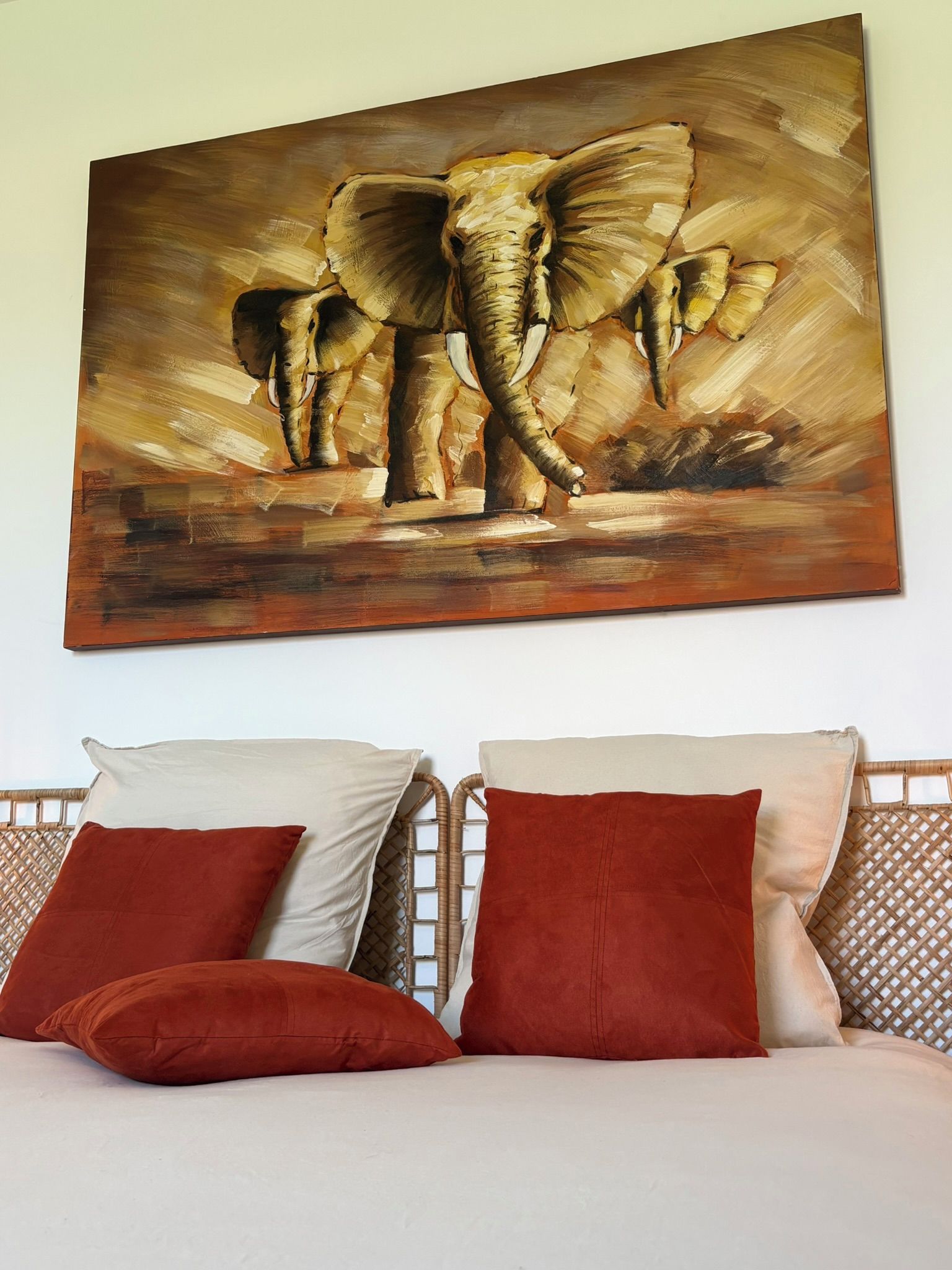 Un lit avec deux oreillers, une tête de lit et un tableau représentant des éléphants accroché au mur.