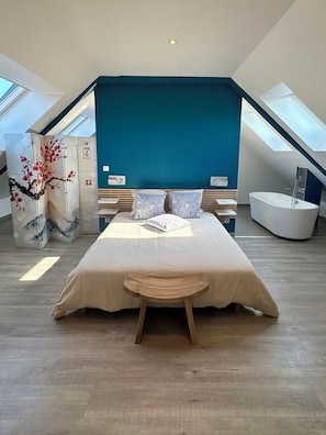 A modern bedroom with a large bed, a skylight, and a bathtub.