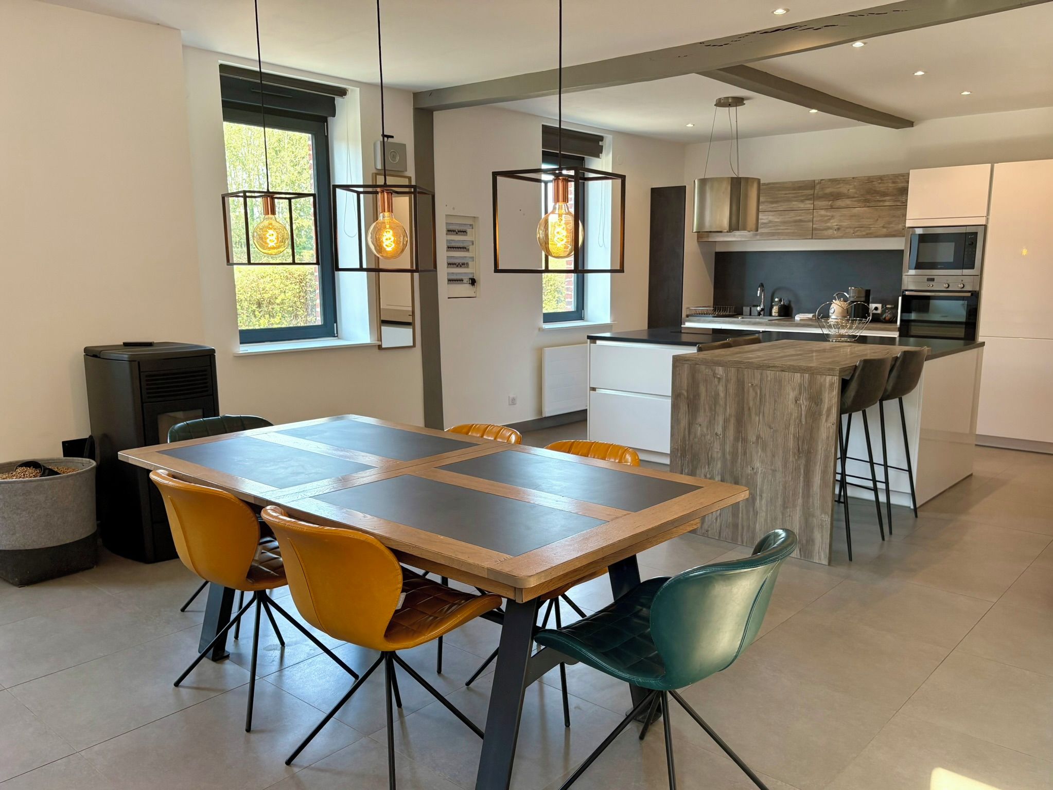 Een moderne keuken met een centraal eiland, een eethoek met een tafel en stoelen, en hangende lampen.