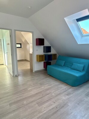 A modern living room with a teal sofa, wooden flooring, and a skylight.