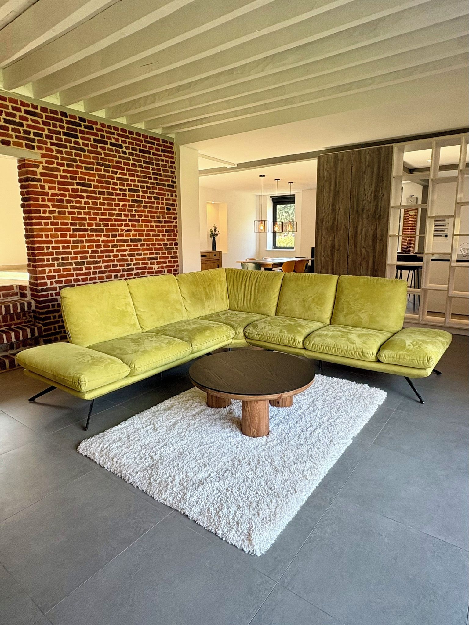 Un salon moderne avec un canapé d’angle vert, une table basse ronde et un tapis à poils longs blanc.