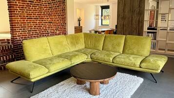 Un salon moderne avec un canapé d’angle vert, une table basse ronde et un tapis à poils longs blanc.