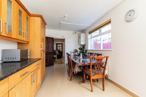 A kitchen with wooden cabinets, a microwave, and a dining area with chairs and a table. - Contractor-Ready 7BR Bristol Home | Parking + WiFi (Bristol)