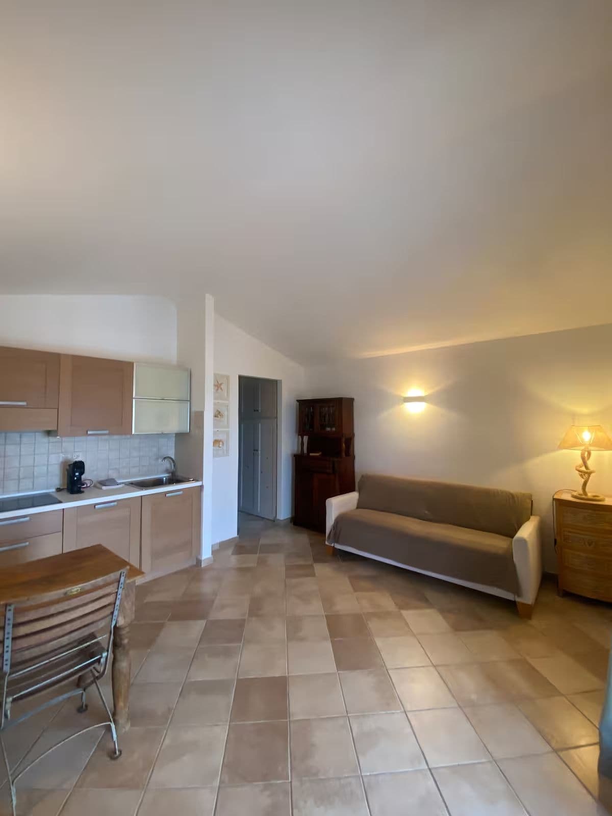 Een ruime woonkamer met een bank en een eettafel, een kitchenette met kastjes, en een betegelde vloer.