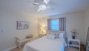 A bedroom with a bed, a nightstand, a chair, a ceiling fan, and a window with curtains. - Beautiful Remodeled 3 Bedroom Pool House (Naples)