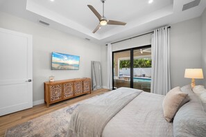 A bedroom with a bed, a nightstand, a ceiling fan, a window with curtains, and a view of a pool. - Refined Coastal 4 Bedroom/4 Bathroom Home with Pool, Spa & Outdoor Kitchen (Naples)