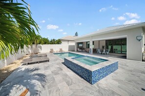 A modern outdoor pool area with a tiled deck, lounge chairs, and a covered patio. - Refined Coastal 4 Bedroom/4 Bathroom Home with Pool, Spa & Outdoor Kitchen (Naples)