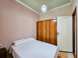 Ein Schlafzimmer mit einem Bett, einem Holzschrank, einer weißen Tür und einer Pendelleuchte.