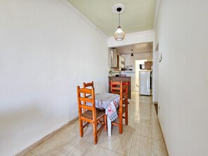 A narrow hallway leading to a kitchen with a dining table and chairs. - Apto com Garagem e Varanda no Jardim Casa Branca (Betim)