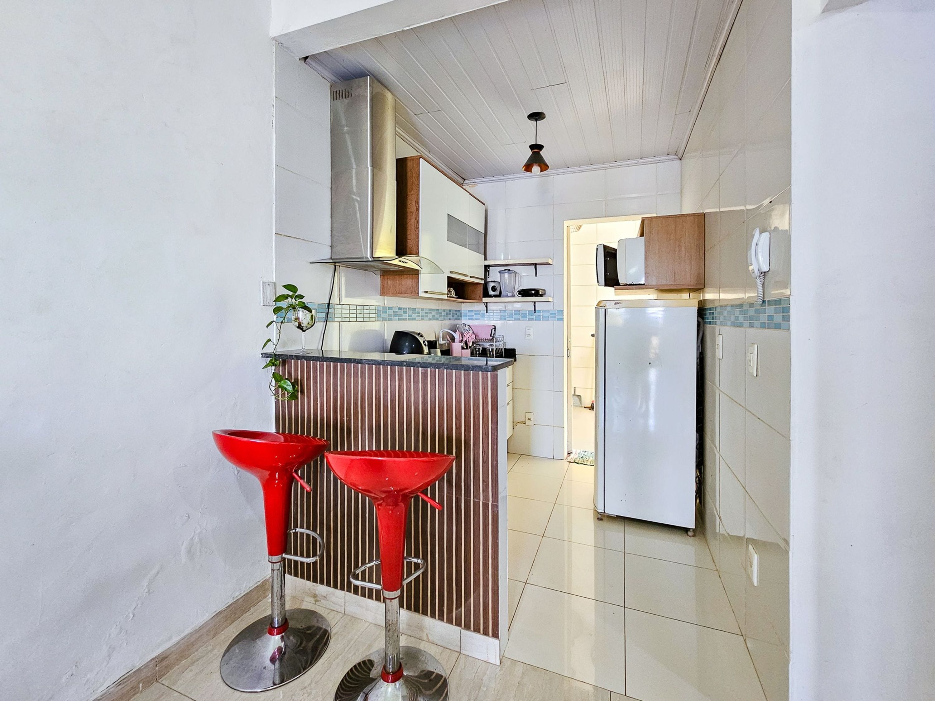 A kitchen with a refrigerator, a microwave, and a sink. There are two red bar stools and a potted plant.