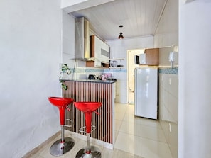 A kitchen with a refrigerator, a microwave, and a sink. There are two red bar stools and a potted plant. - Apto com Garagem e Varanda no Jardim Casa Branca (Betim)