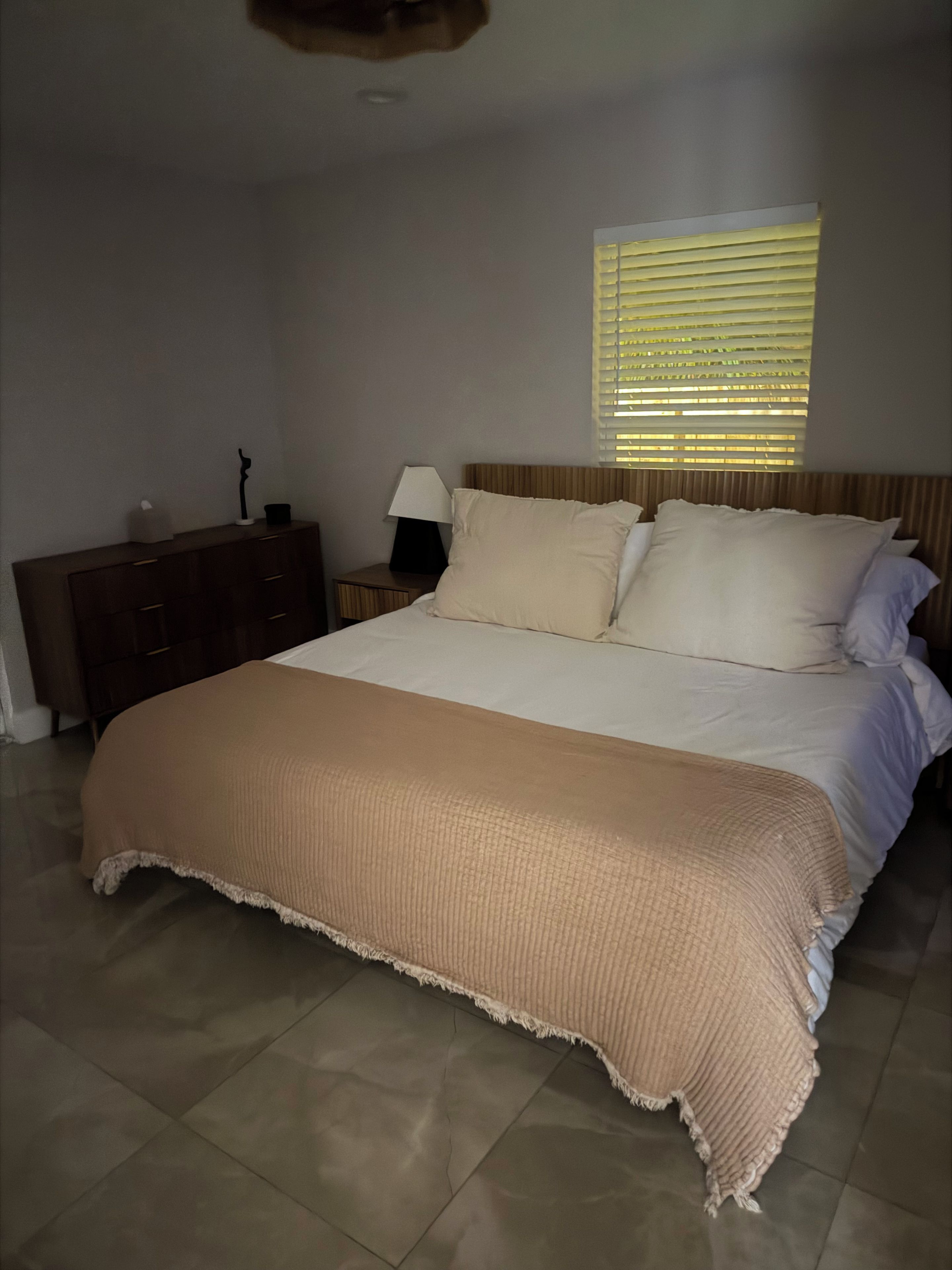 Un dormitorio con cama, mesita de noche, lámpara y ventana con persianas.
