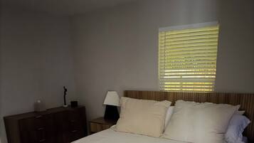 Un dormitorio con cama, mesita de noche, lámpara y ventana con persianas.
