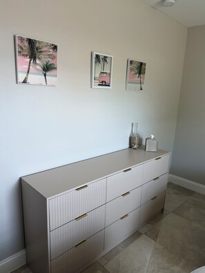 Ein modernes Zimmer mit einem großen weißen Schrank, drei gerahmten Bildern an der Wand und einer kleinen Vase mit einem Taschentuchhalter darauf.