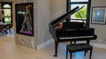 A grand piano in a spacious room with a marble floor, a framed artwork on the wall, and a dining area in the background.