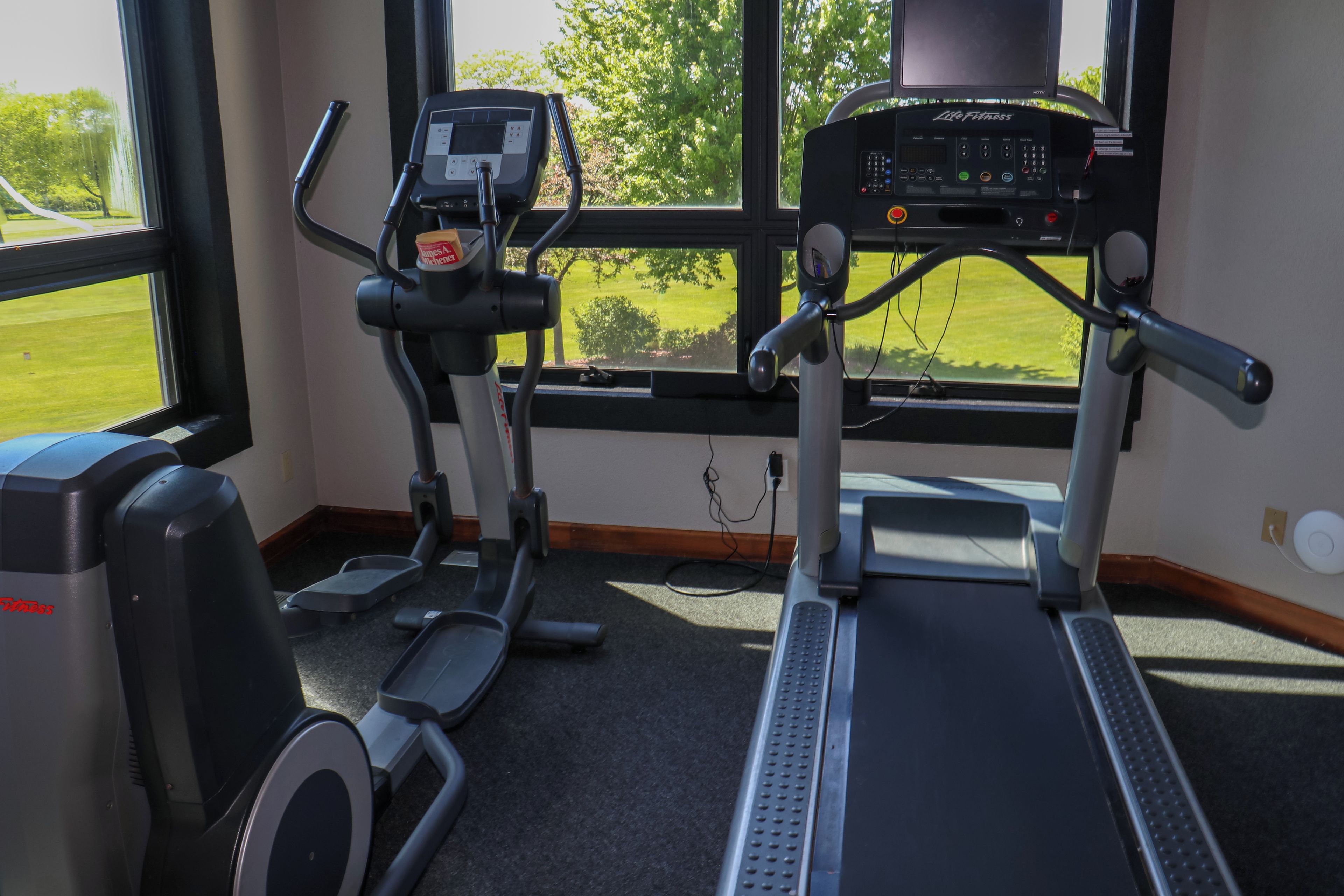 Gimnàs amb equip de cardio, incloent cintes de córrer i una el·líptica, i una panca de peses.